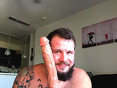 Tattooed solo guy spreads his legs to ride a massive dildo at home